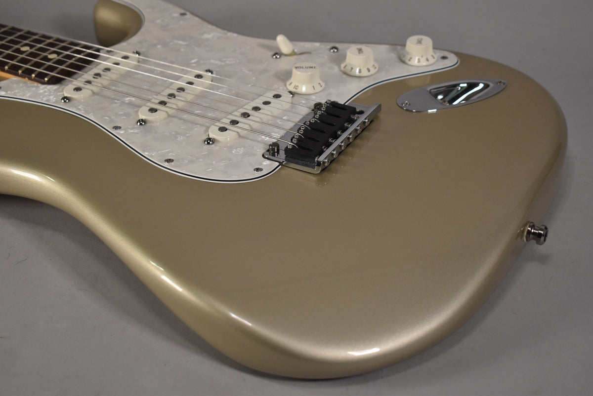 Close-up of a gold electric guitar body with a pearloid pickguard, three single-coil pickups, and a tremolo bridge.