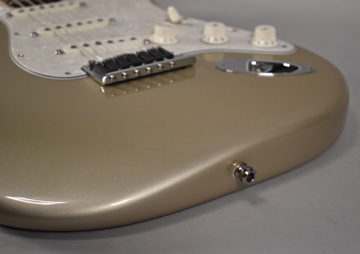 The lower bout of a metallic gold Stratocaster, showing the output jack, bridge, and three cream control knobs on a pearloid pickguard.
