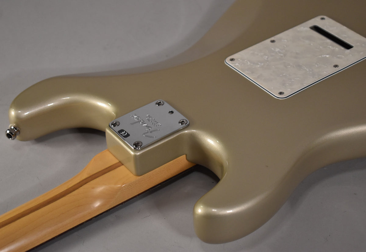Back of a gold Stratocaster showing the neck plate with "Fender" logo, neck heel, output jack, and pearloid tremolo cover.