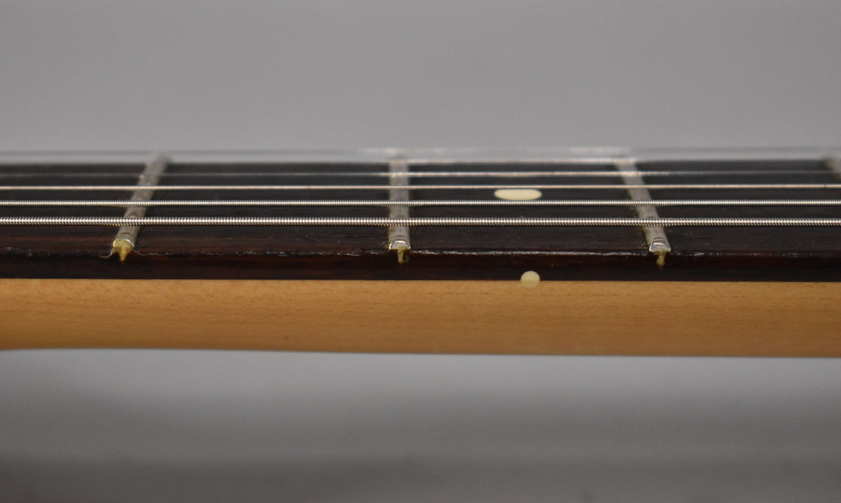 Close-up of the rosewood fretboard and maple neck, showing light wear on the frets and a small chip near the 5th fret.