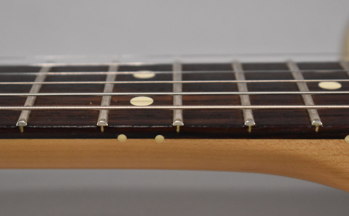 Close-up of the dark rosewood fretboard and light maple neck, showing light wear on the frets and side dots.