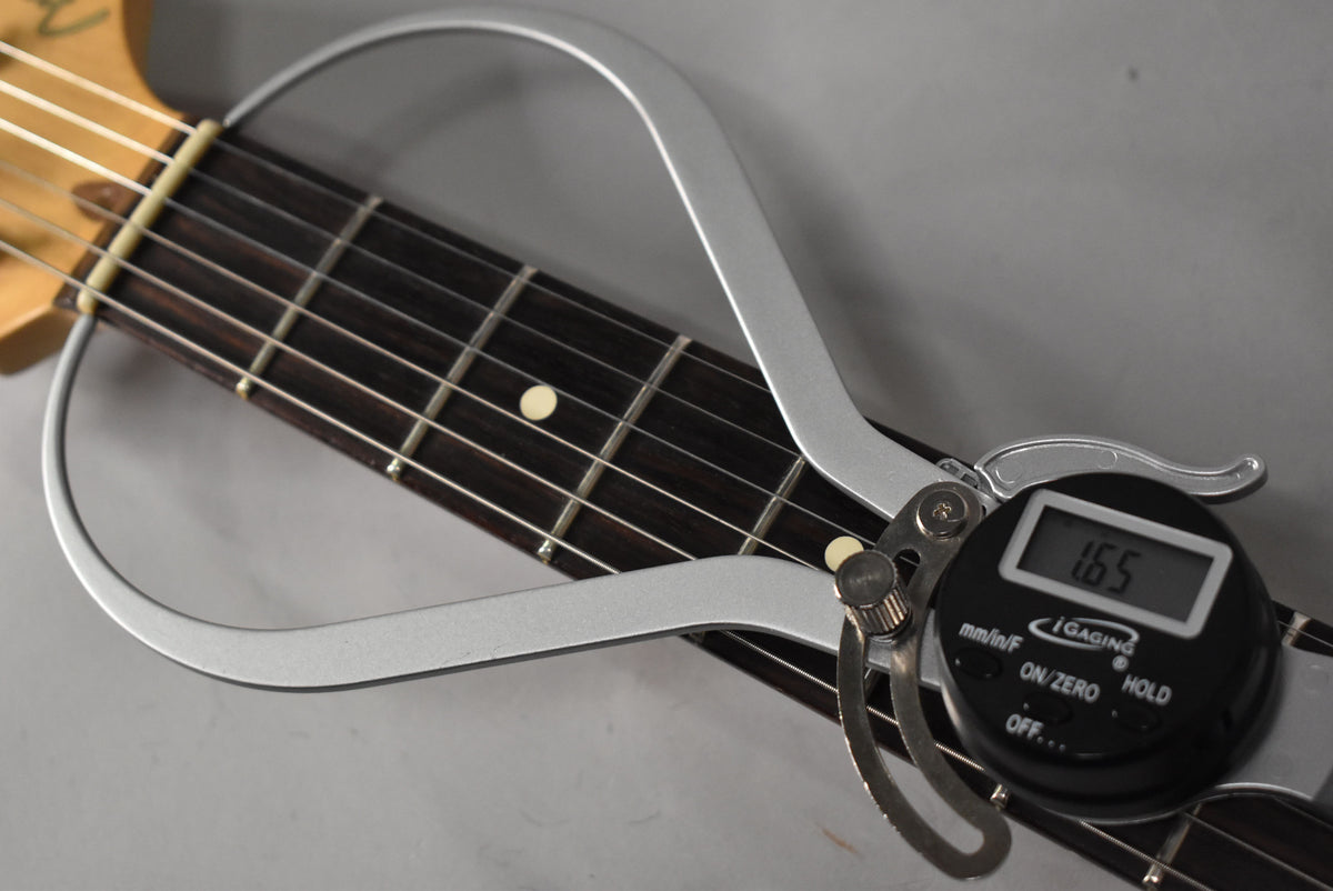 A digital fret height gauge measures the dark fretboard with light dot inlays and metal frets, showing "1.65" on its screen.
