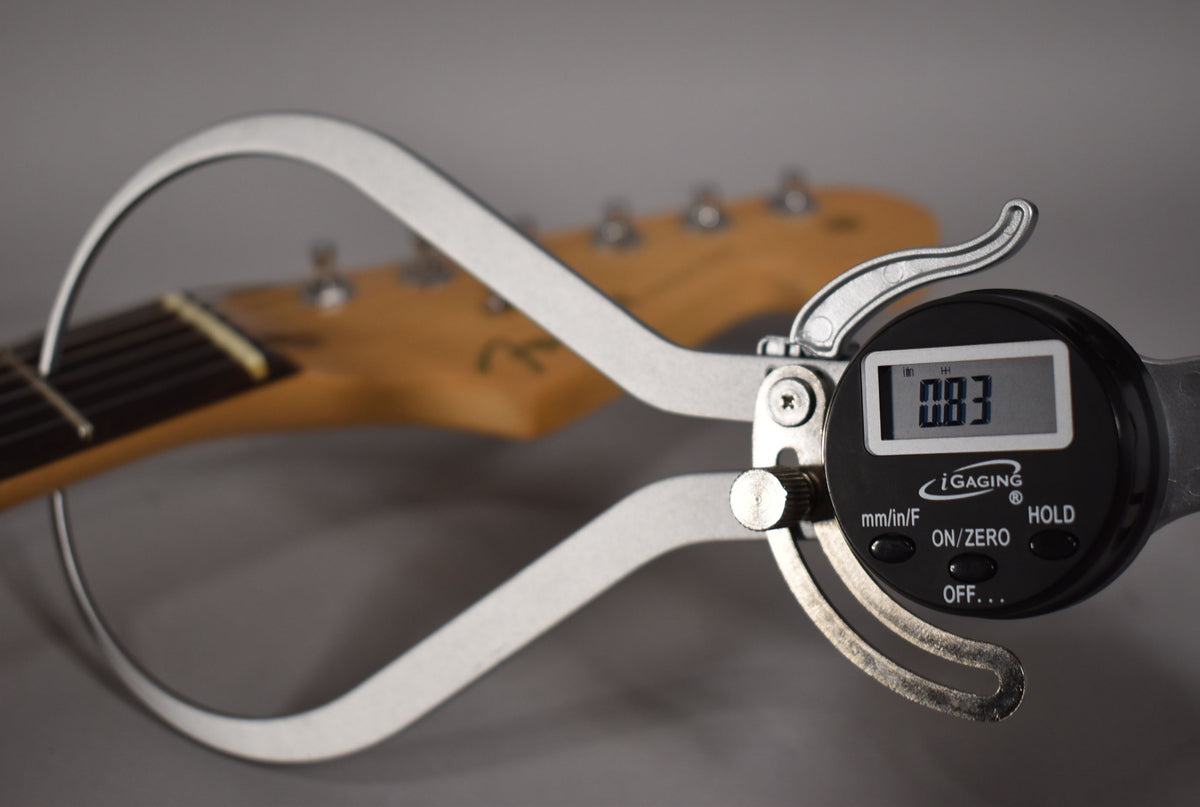 Digital calipers measure the guitar's neck relief at 0.83, with the headstock and tuning pegs blurred in the background.