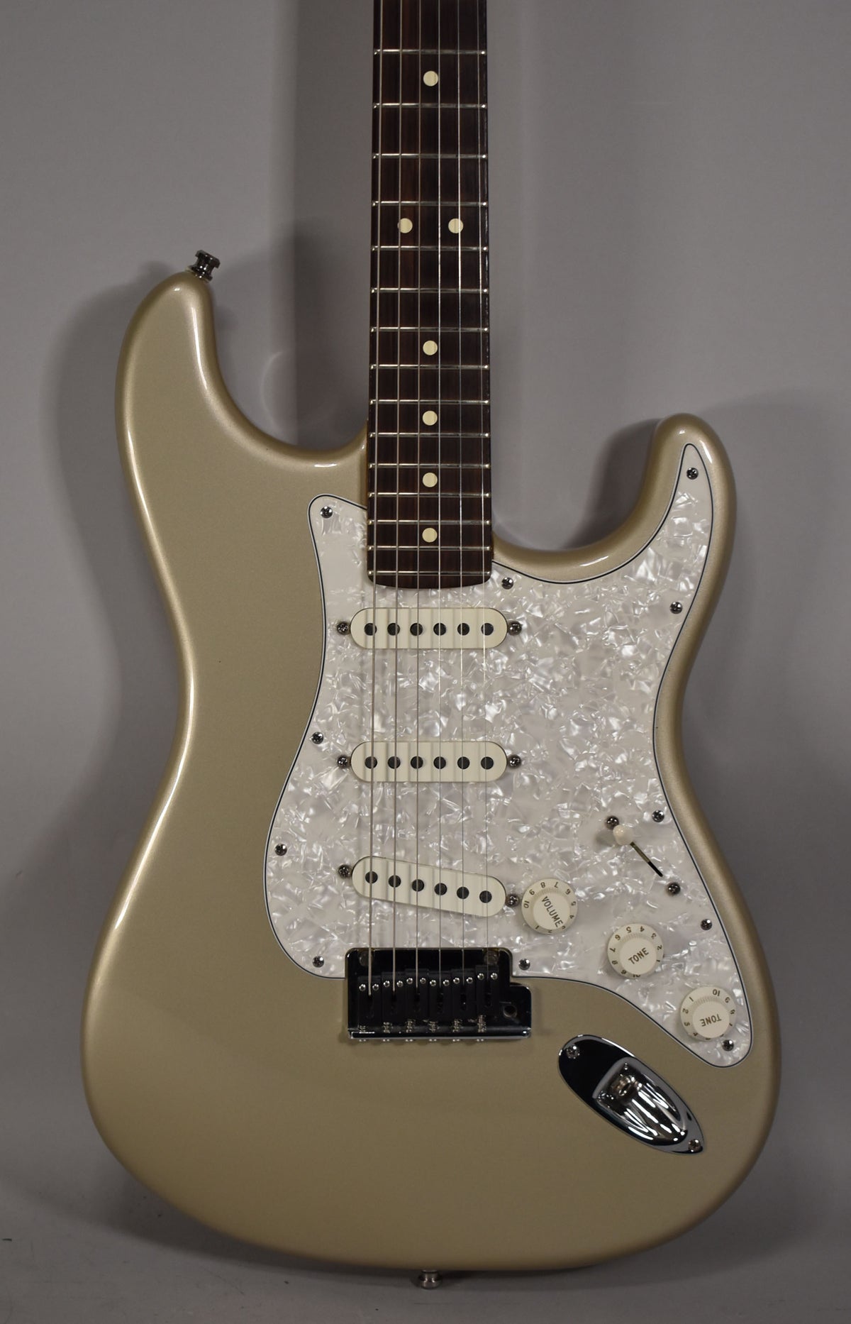Full-body shot of a metallic gold Stratocaster with a pearloid pickguard, three single-coil pickups, and a rosewood fretboard.