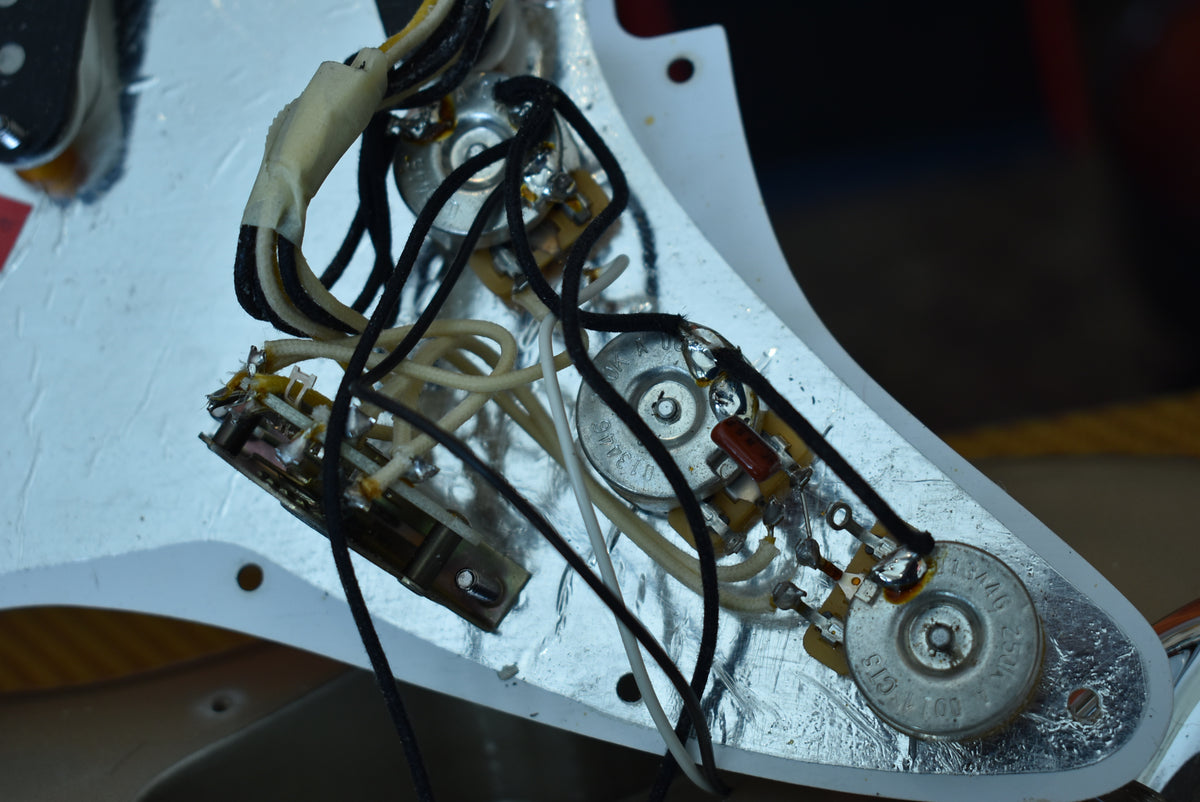 Close-up of the guitar's internal wiring, showing three potentiometers, a switch, and various wires on a silver plate.
