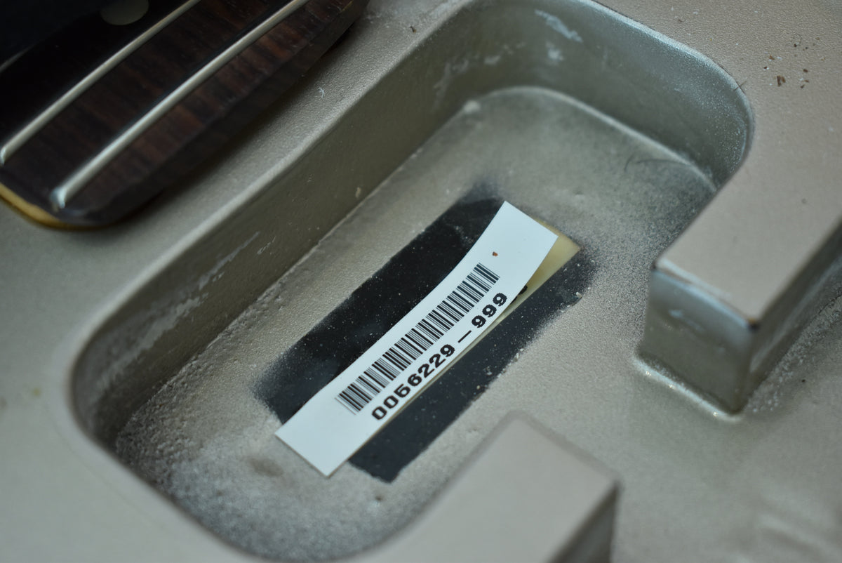 A barcode sticker with "0066229-999" is visible in a guitar's body cavity, next to a dark wood fretboard.
