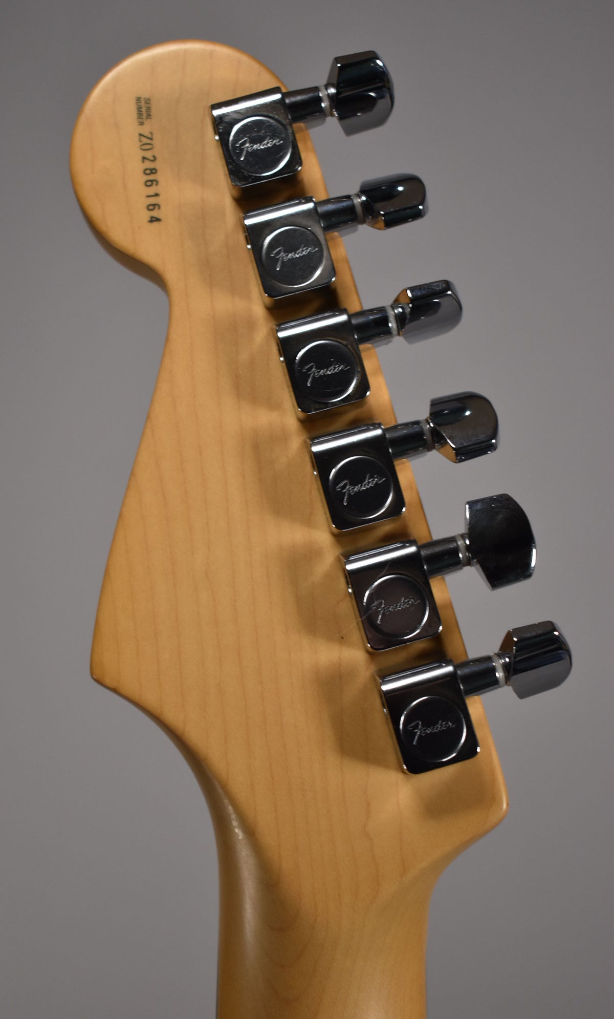 The back of a light wood headstock with six chrome tuners, angled slightly from the left.