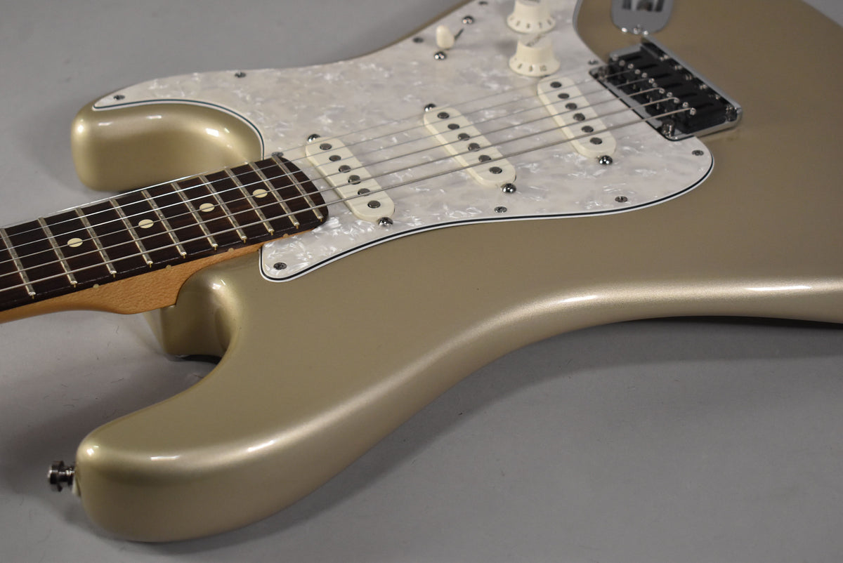 Close-up of a gold electric guitar body with a pearloid pickguard, three single-coil pickups, and part of the fretboard.