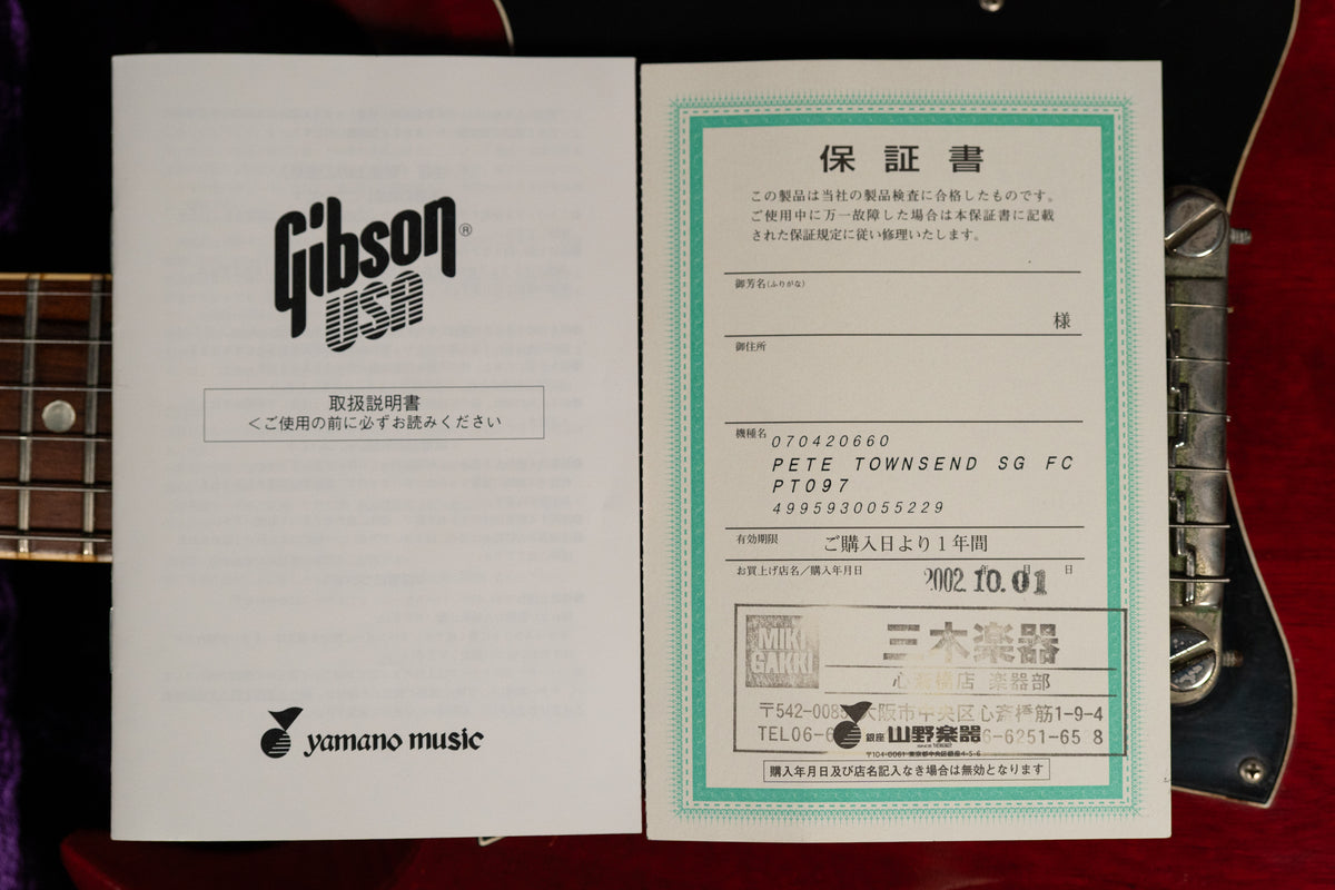 Two white documents with Japanese text, one with a green border, rest on a dark red guitar body with chrome hardware.