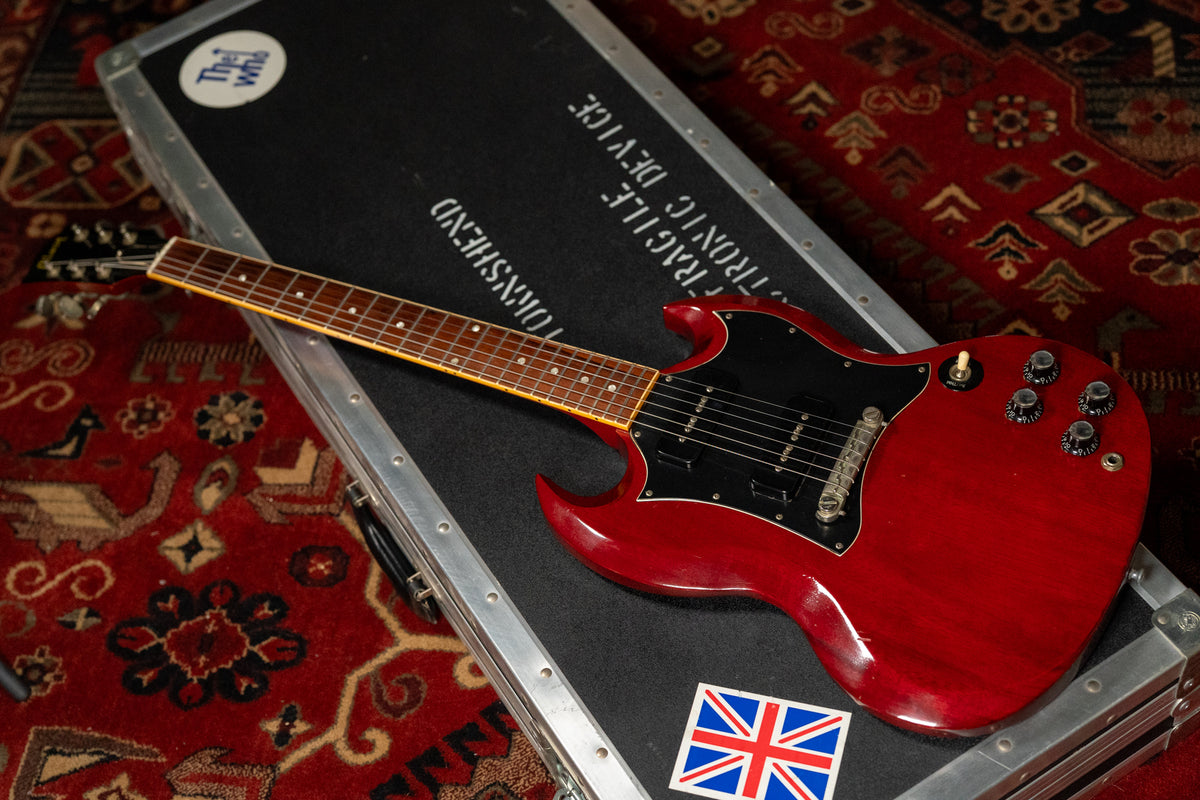 A cherry red SG Special with black pickguard and P90 pickups rests on its black flight case, angled left.