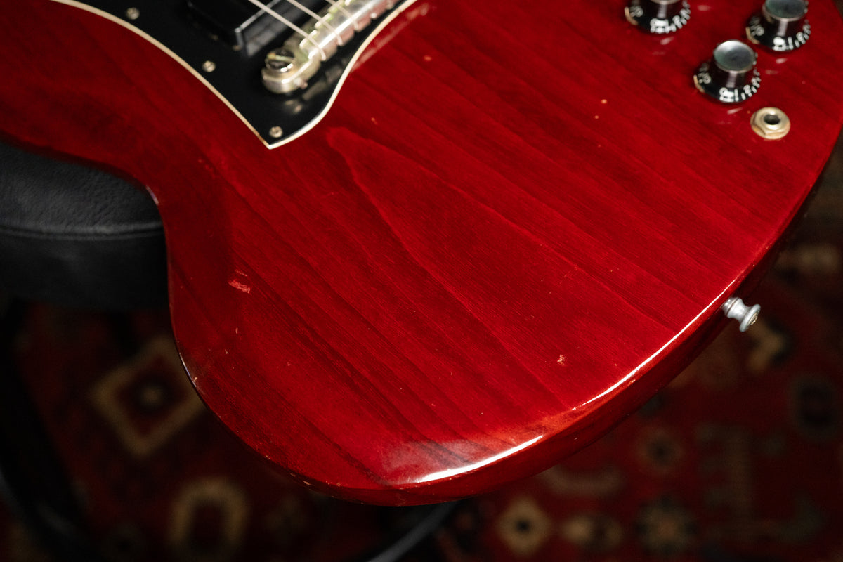 Close-up of the SG's cherry red body, showing wood grain, a few small dings, and three black control knobs with silver tops.