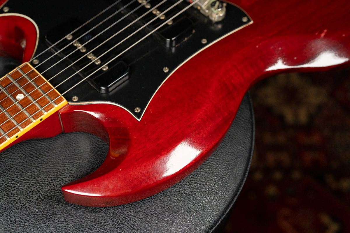 The cherry red SG body, with a black pickguard and two humbuckers, shows light wear and finish checking on the lower bout.