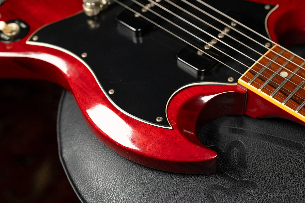 Close-up of the cherry red SG's lower horn and black pickguard, showing light wear and a small chip near the strap button.
