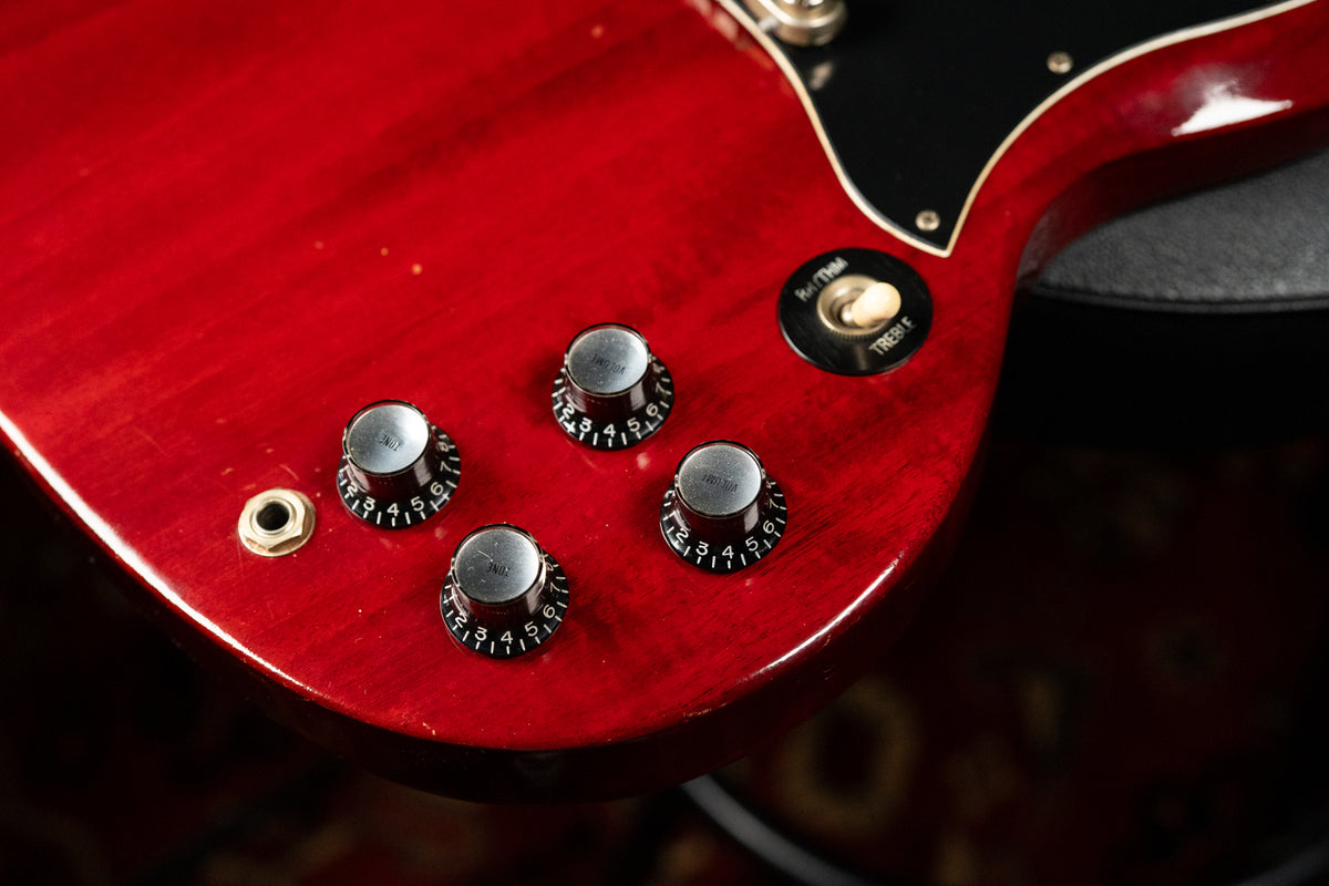 Close-up of the cherry red guitar body, showing four black numbered control knobs, a cream toggle switch, and a black pickguard.