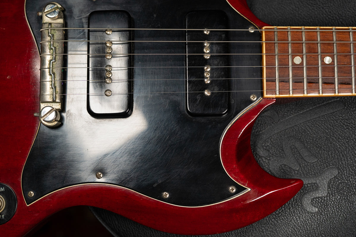Close-up of the cherry red SG body, showing the worn black pickguard, two P90 pickups, and a tune-o-matic bridge.