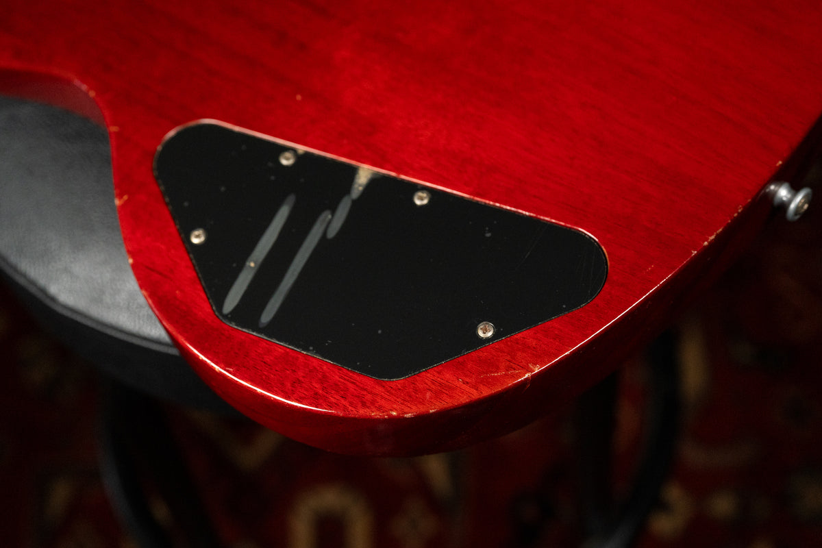 Close-up of the guitar's cherry red body, showing a black control cavity cover with scratches and wear along the body's edge.