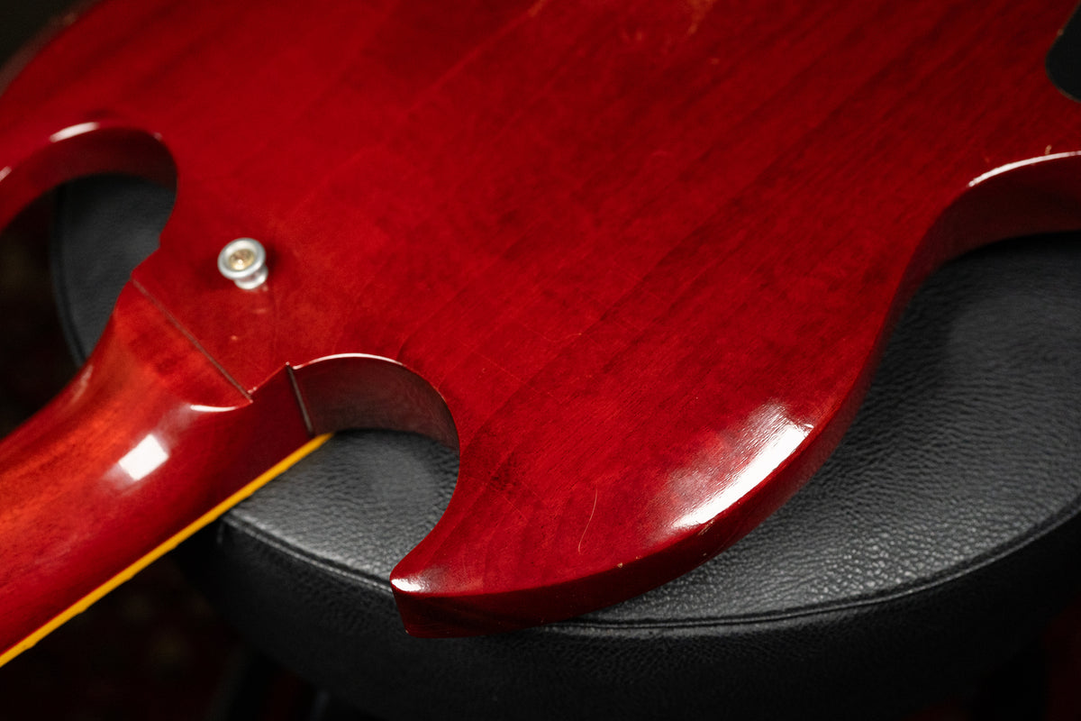 Close-up of the SG's cherry red body and neck joint, showing light scratches and a chrome strap button on the upper horn.