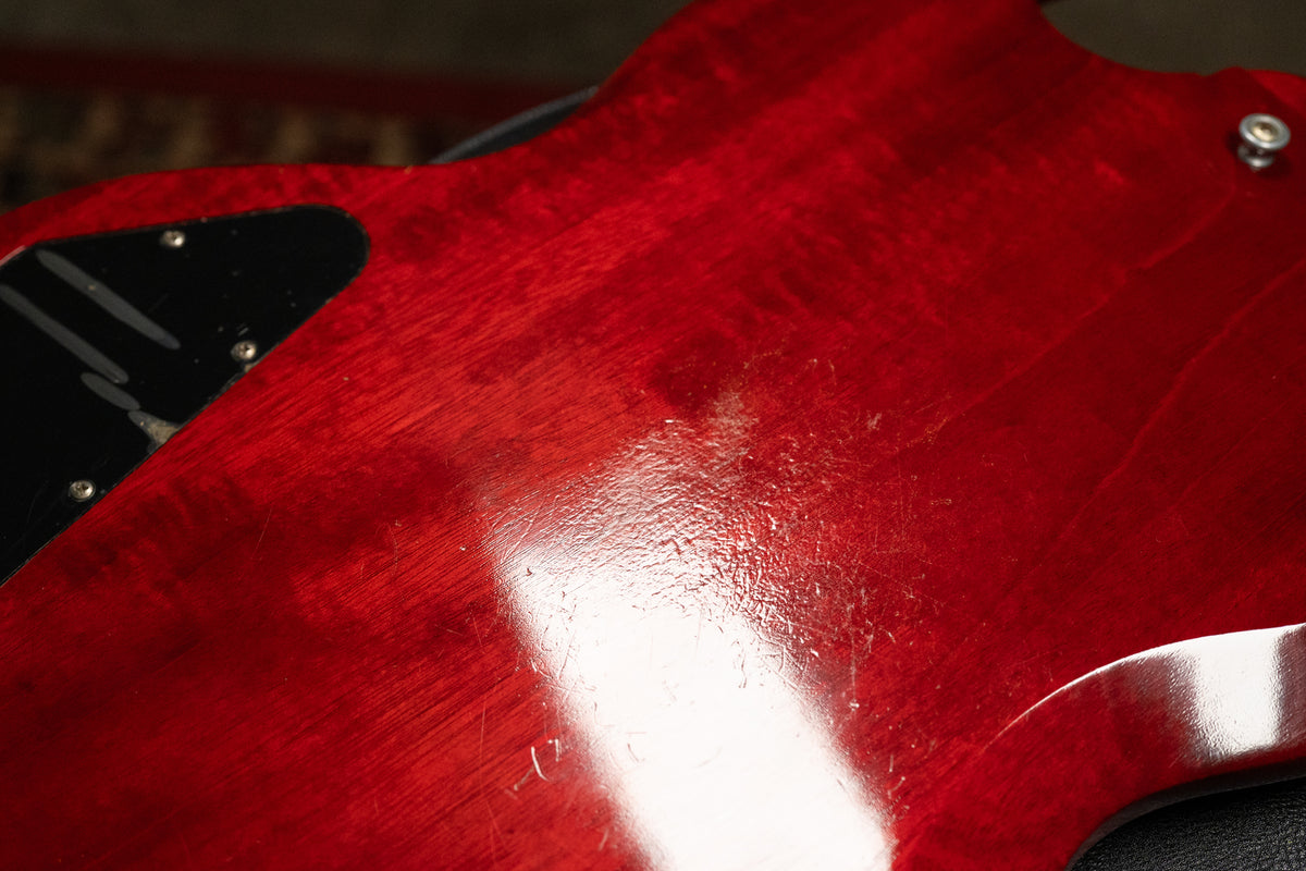 Close-up of the guitar's cherry red back, showing heavy finish wear, scratches, and checking, with a black control plate visible.