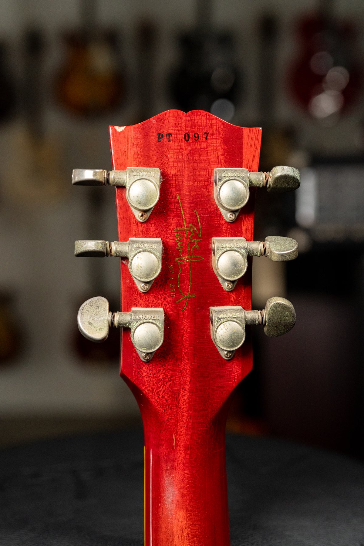The back of a red guitar headstock and neck, showing six tarnished Grover tuners and a gold signature.