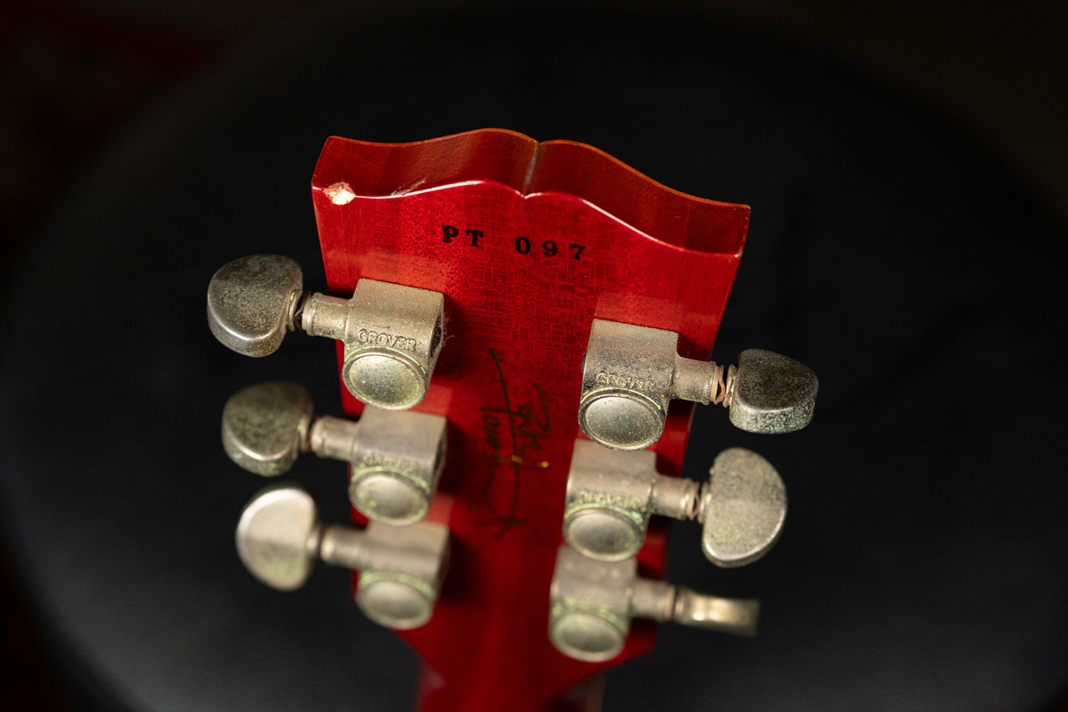 The back of a cherry red headstock with six tarnished Grover tuners, showing a chip on the top edge and "PT 097" stamped.