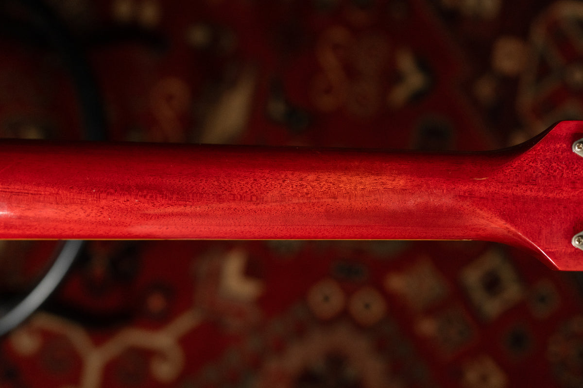 The back of the guitar's cherry red neck shows subtle wood grain and light finish wear, with three tuning machine screws visible.