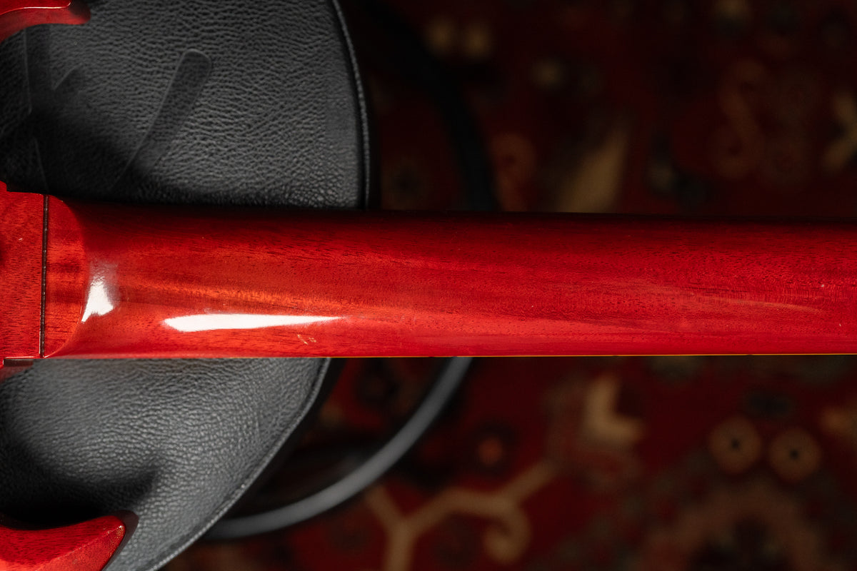 Overhead view of the guitar's cherry red neck and heel, showing light wear and wood grain, resting on a black case.