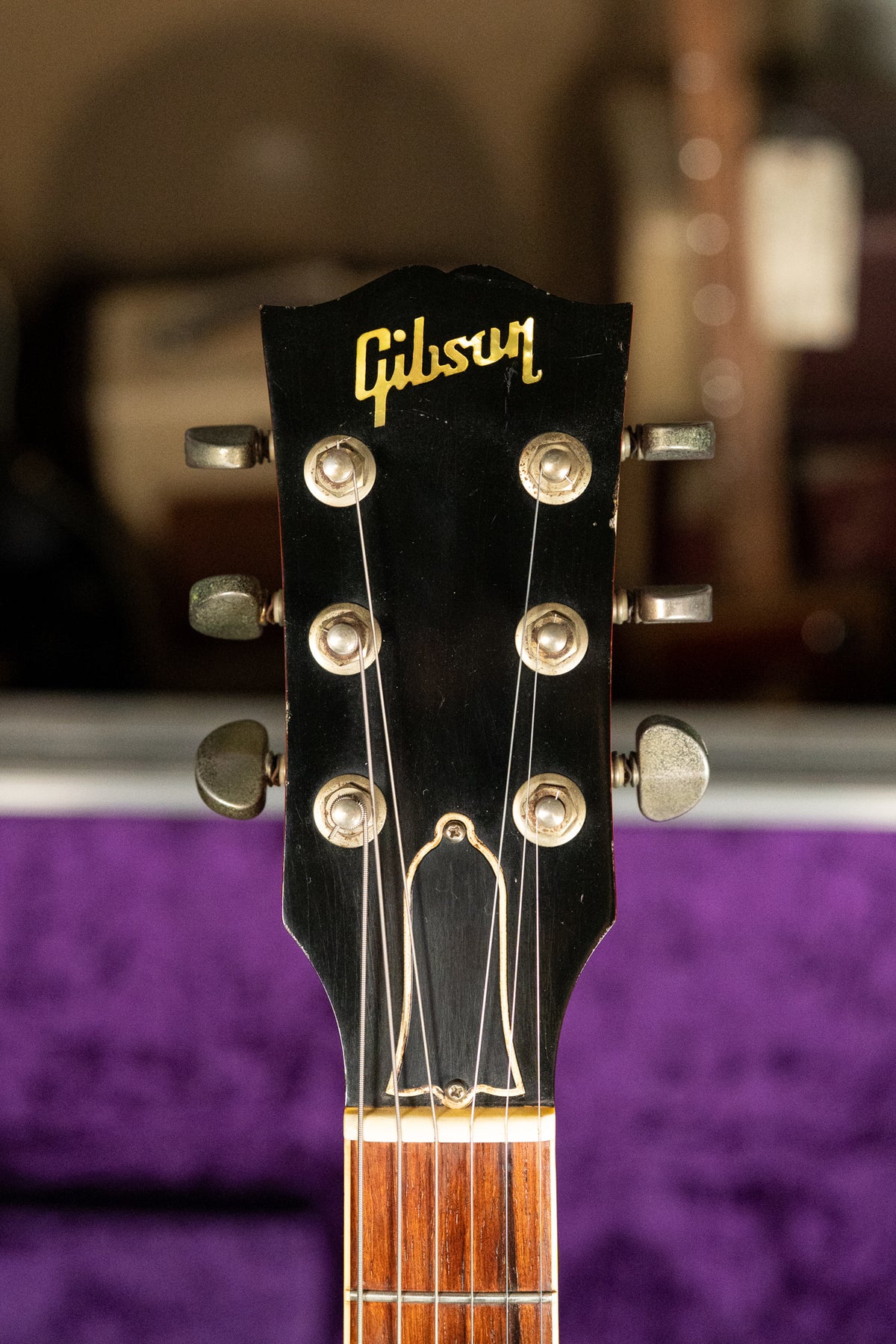 The black headstock, with gold logo and six aged nickel tuners, shows light wear and a glimpse of the rosewood fretboard.
