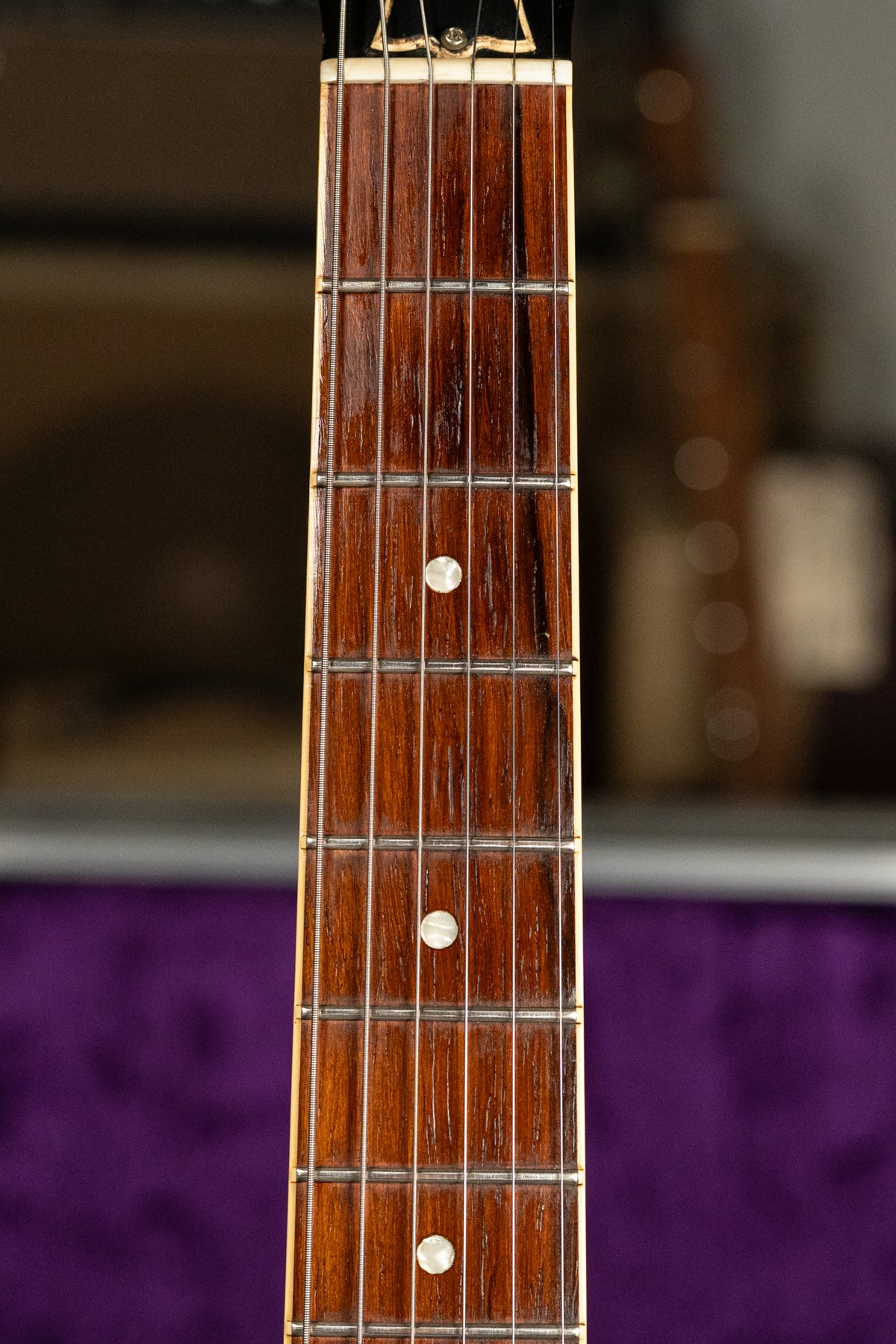 Close-up of the guitar's dark brown rosewood fretboard with mother-of-pearl dot inlays, showing light wear and string marks.