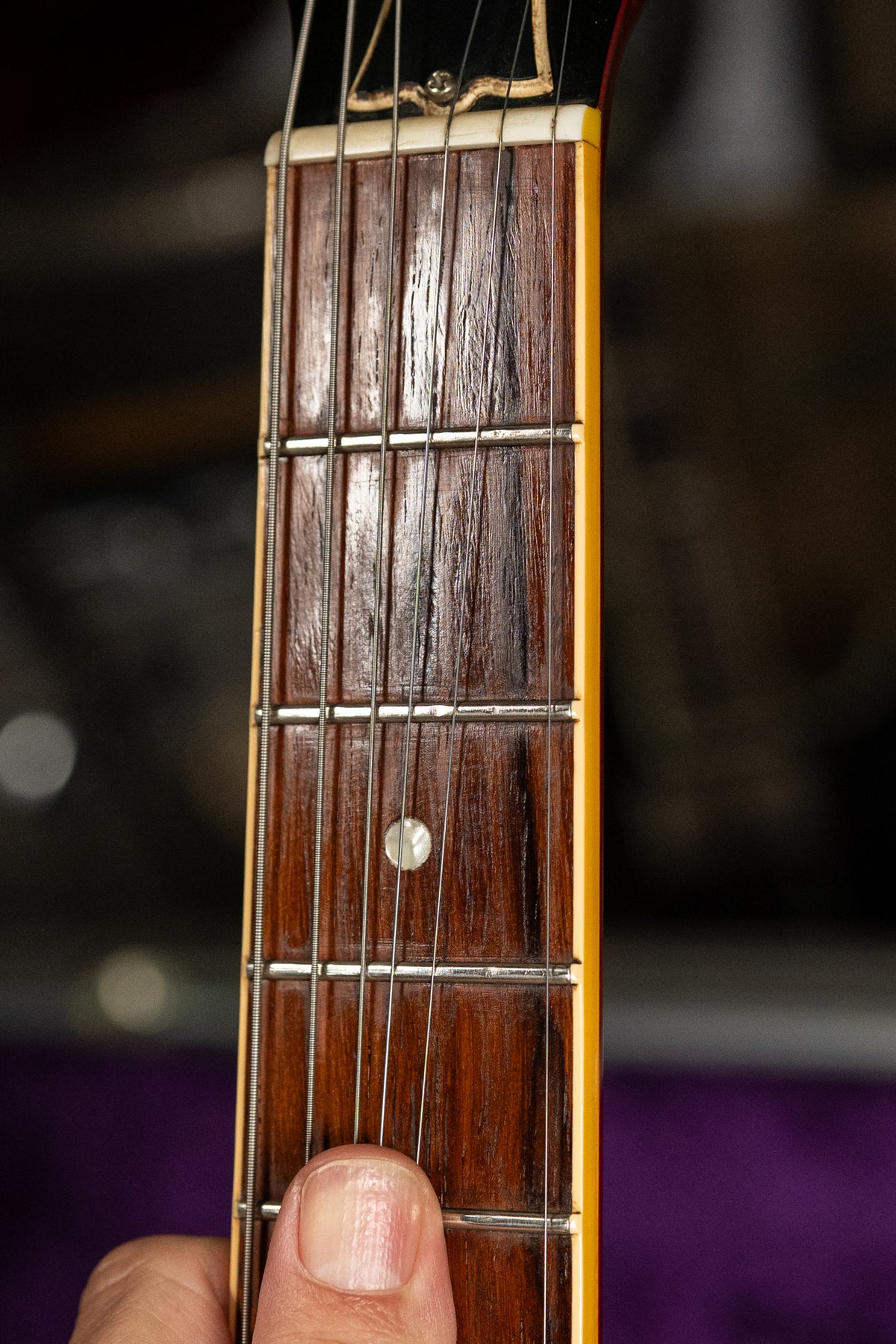 A close-up of the dark rosewood fretboard with a single pearl dot inlay at the 7th fret, showing light wear and a person's thumb.