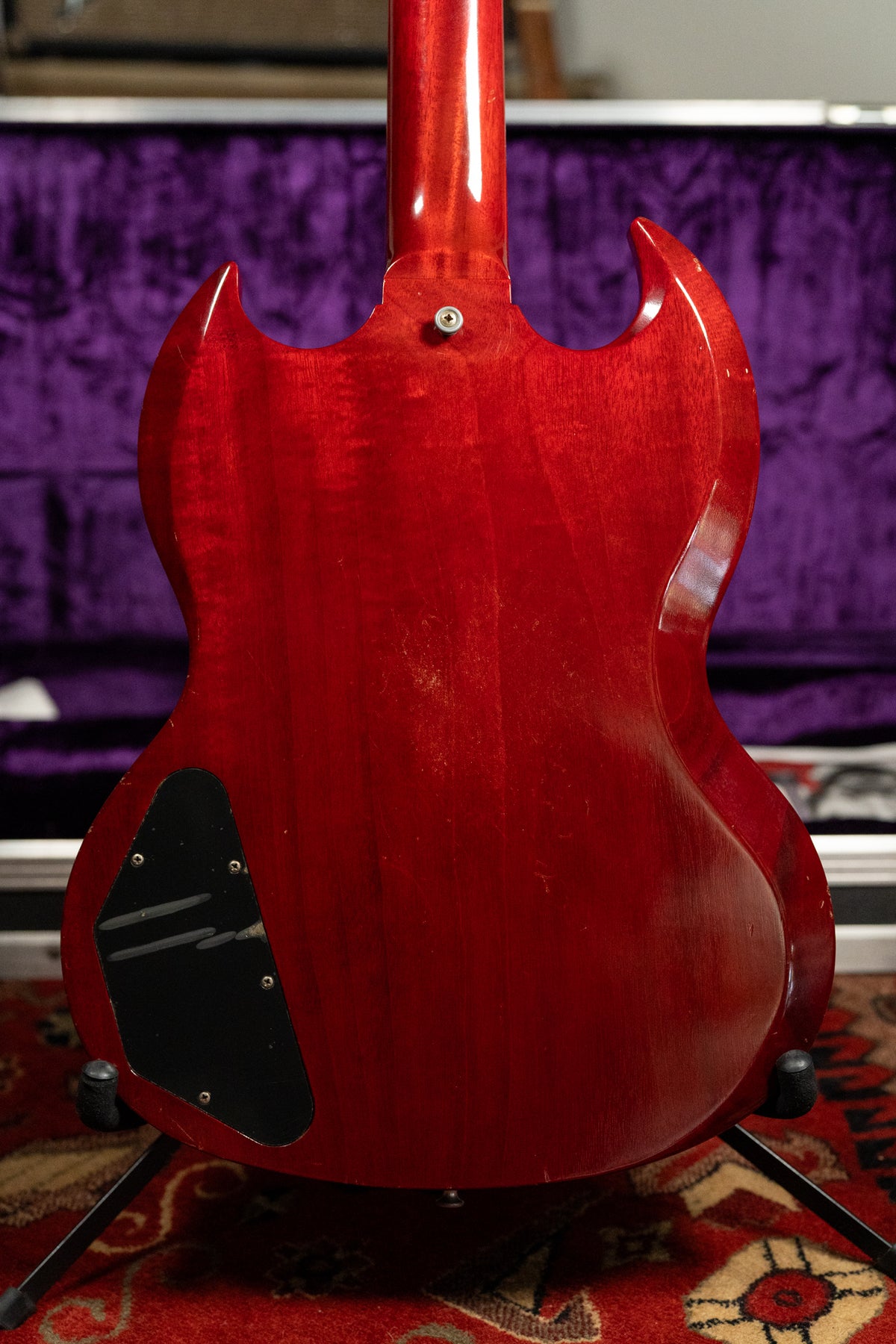 The back of a cherry red SG with a glossy finish, showing light wear and a black control cavity cover.