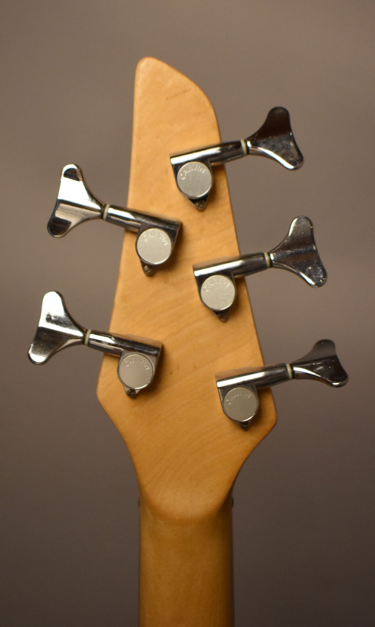 The back of a natural wood headstock with five chrome tuning machines, showing some wear and tarnishing.