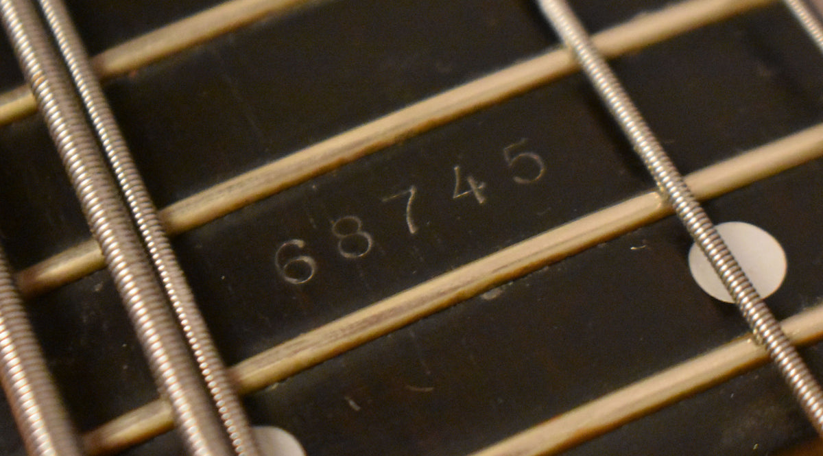 Close-up of the dark fretboard with light frets and strings, showing the serial number "68745" stamped between the frets.