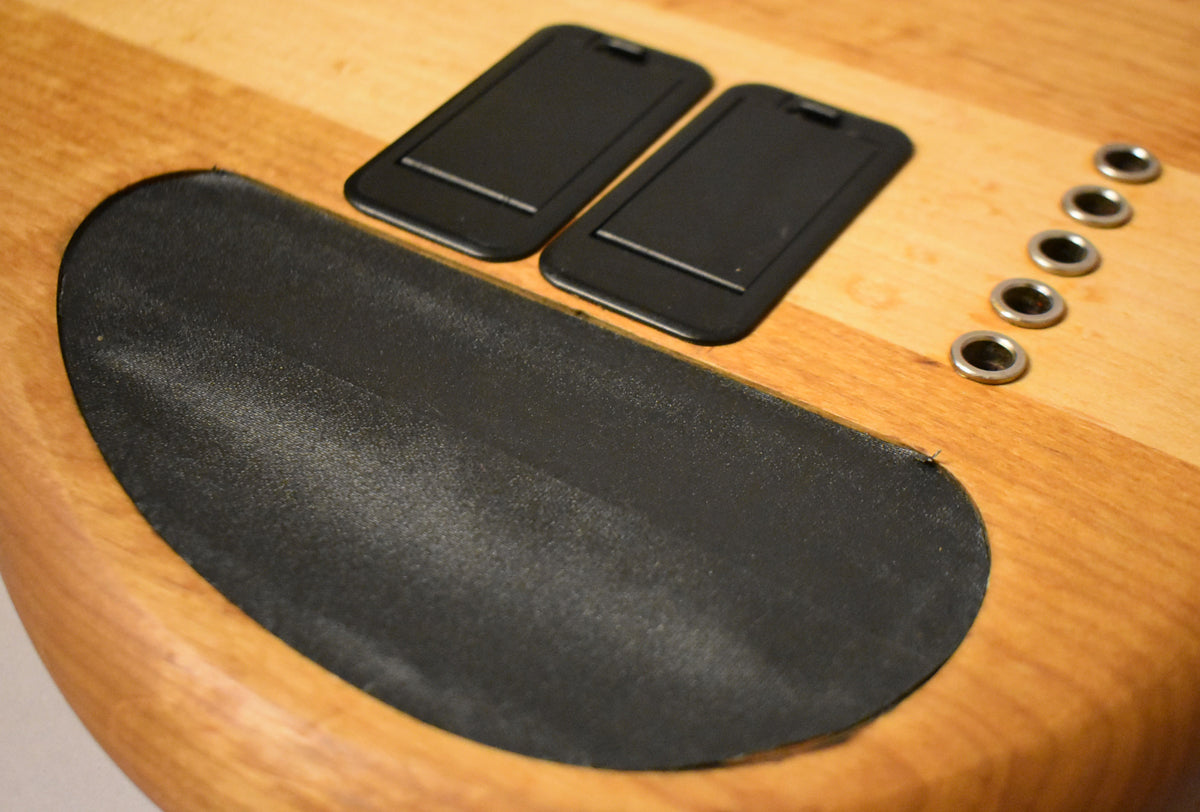 Close-up of the bass's natural wood body, showing two black battery covers, a large black control cavity cover, and five chrome ferrules.