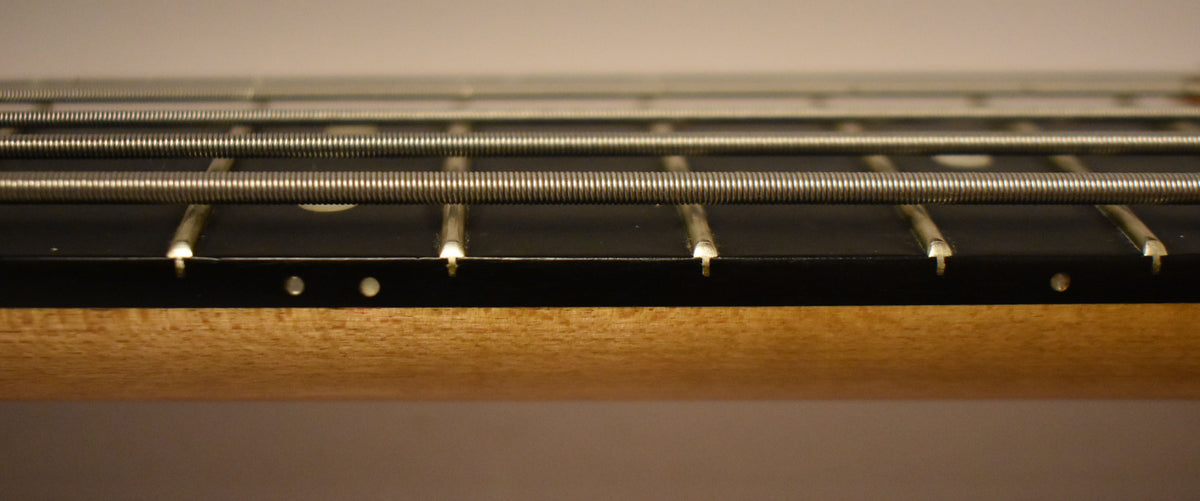 Close-up of the bass's maple neck and black fretboard with five strings, showing white side dots and light fret wear.