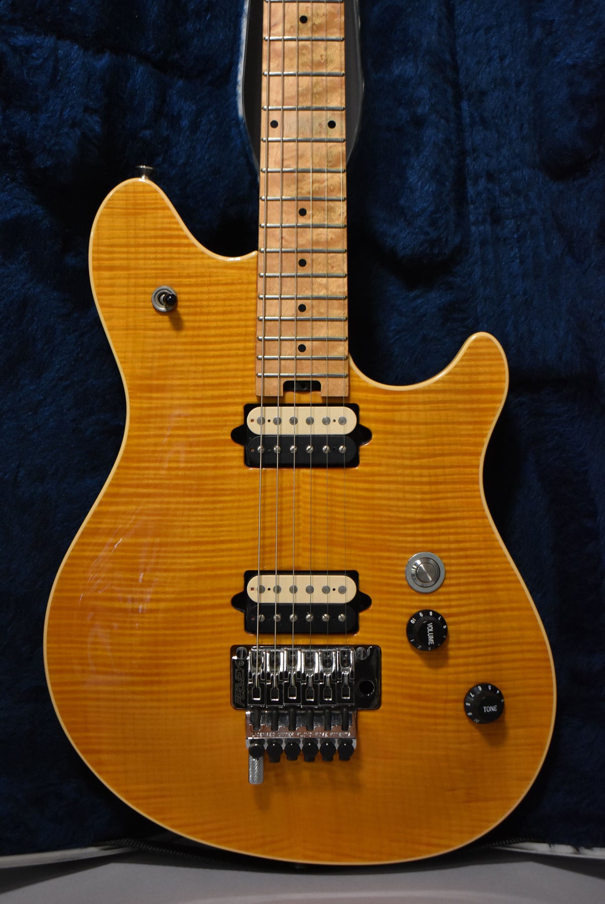 Full-frame view of an amber flamed-maple guitar with a maple fretboard, two cream humbuckers, a Floyd Rose tremolo, and three black knobs.