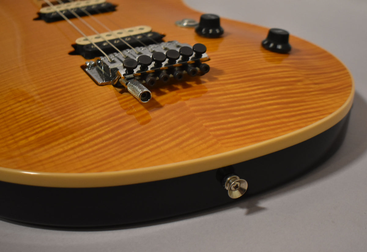 Close-up of the amber flame maple top, showing the tremolo system, two black control knobs, and a strap button on the black body binding.