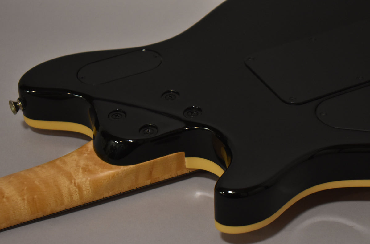 Rear view of the guitar's lower body, showing the black finish with cream binding, a maple neck, and two control cavity covers.