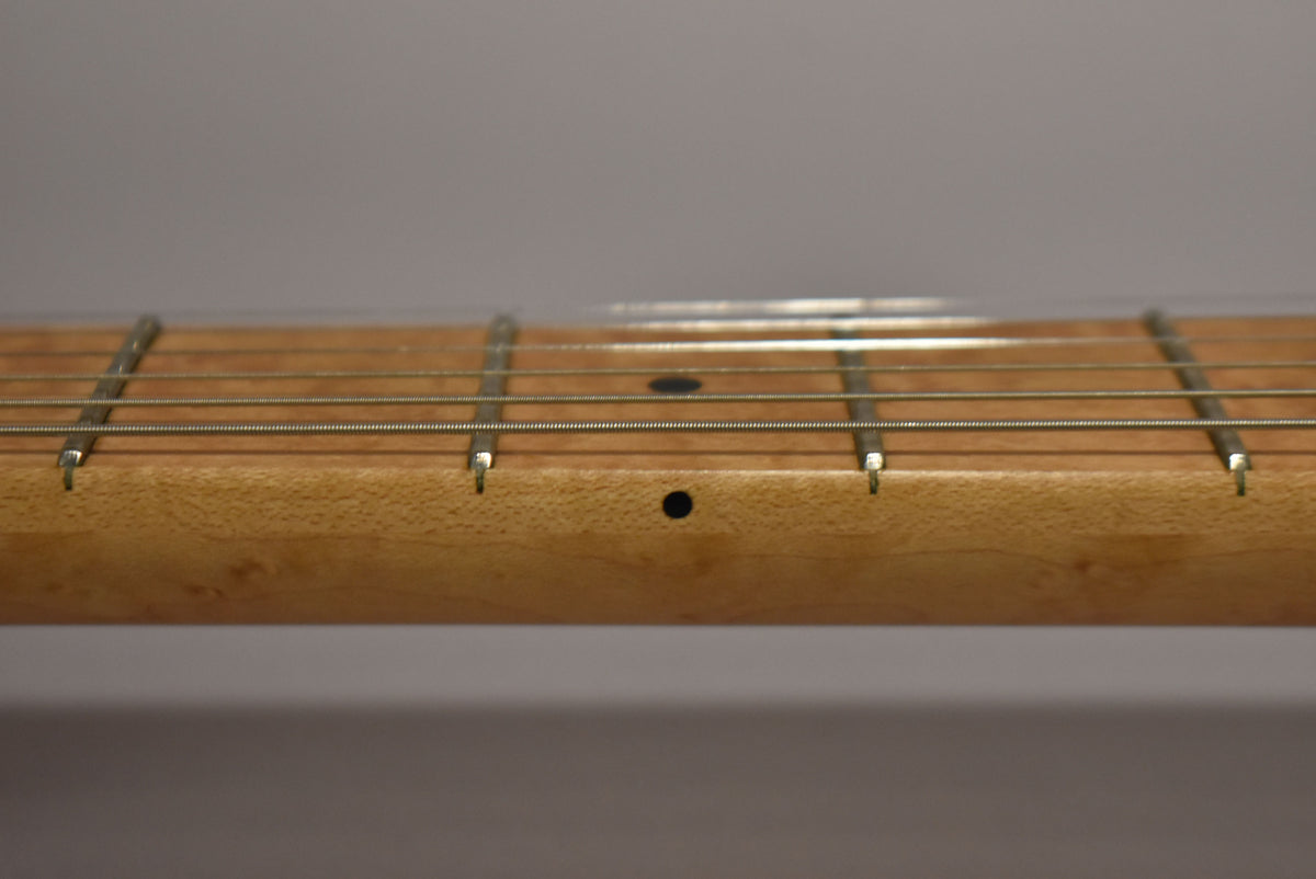 Close-up of the maple fretboard, showing frets 3-7, with black dot inlays on the fretboard and side.