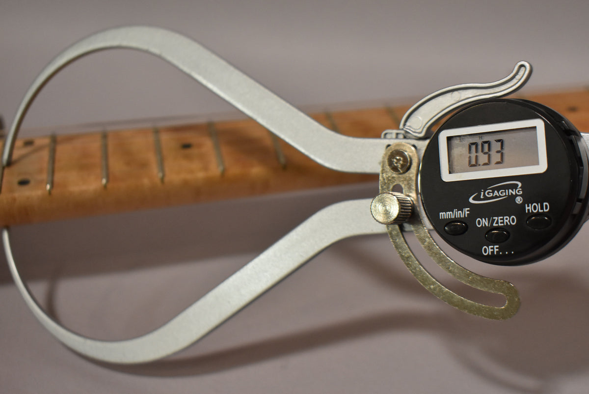 A digital caliper measures the guitar's maple neck, displaying "0.93" on its screen, with fret markers visible.