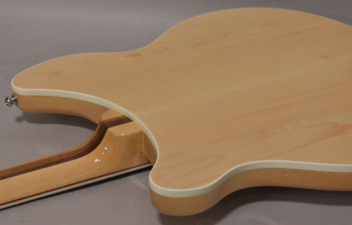 The back of the guitar, showing the light maple body with white binding, a visible neck-through construction, and a strap button.