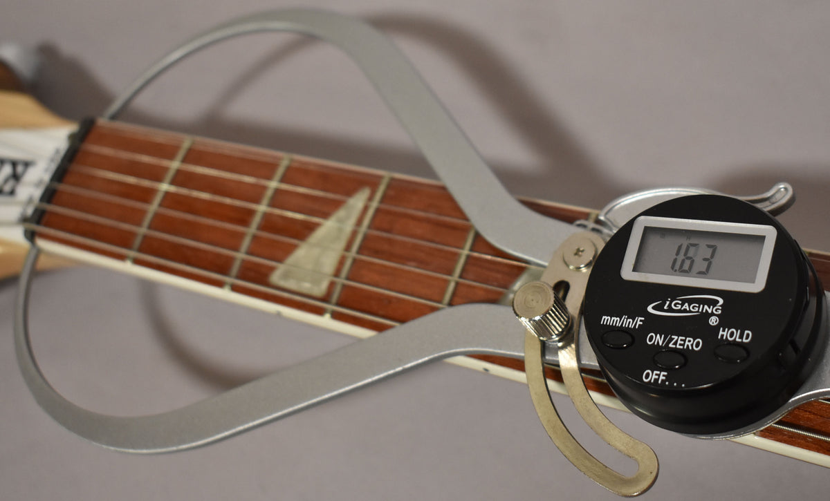 A digital caliper measures the guitar's fretboard, showing a reading of 1.63, with triangular inlays visible.