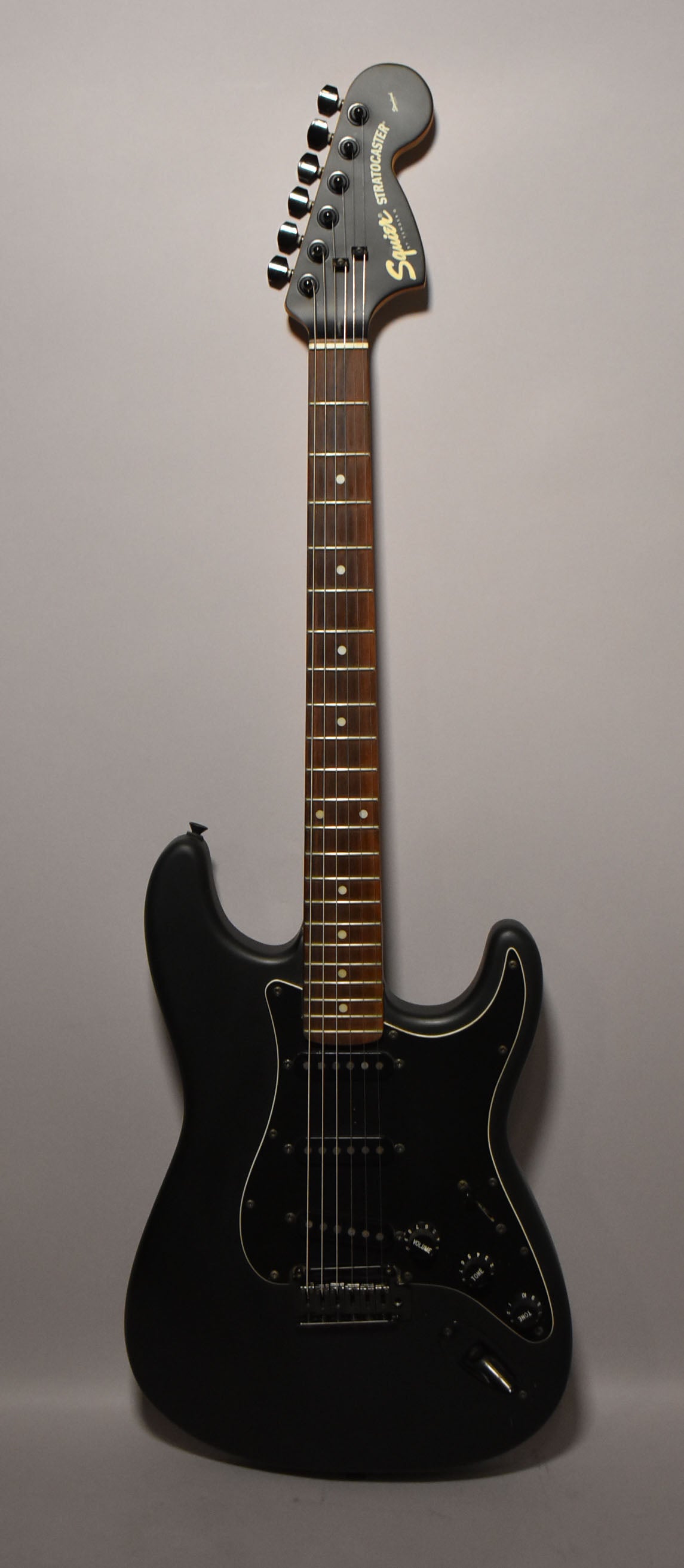 Full-length, front view of a matte black electric guitar with a dark rosewood fretboard, black pickguard, and three black single-coil pickups.