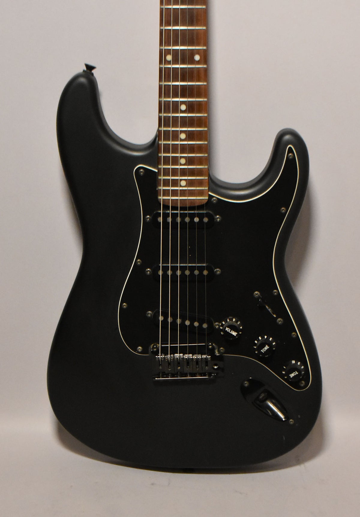 Full-frame view of a matte black Stratocaster with a black pickguard, three single-coil pickups, and black hardware.