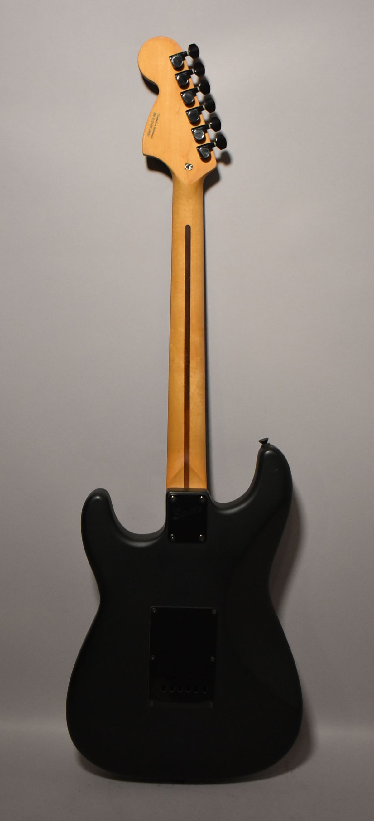 Full rear view of a satin black solid body guitar with a maple neck, black tuners, and a black tremolo cover.