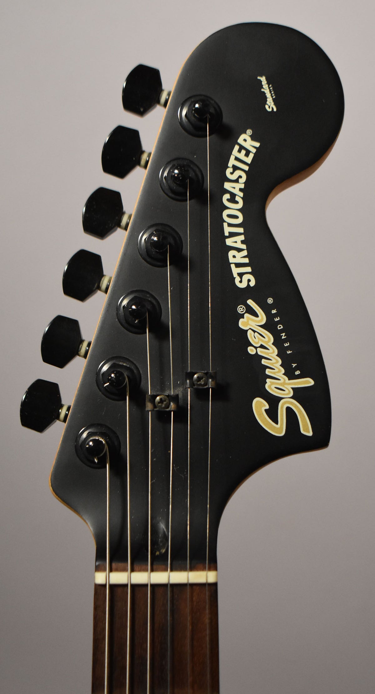 Close-up of the black satin headstock, angled slightly right, showing six black tuners, string trees, and a cream nut.