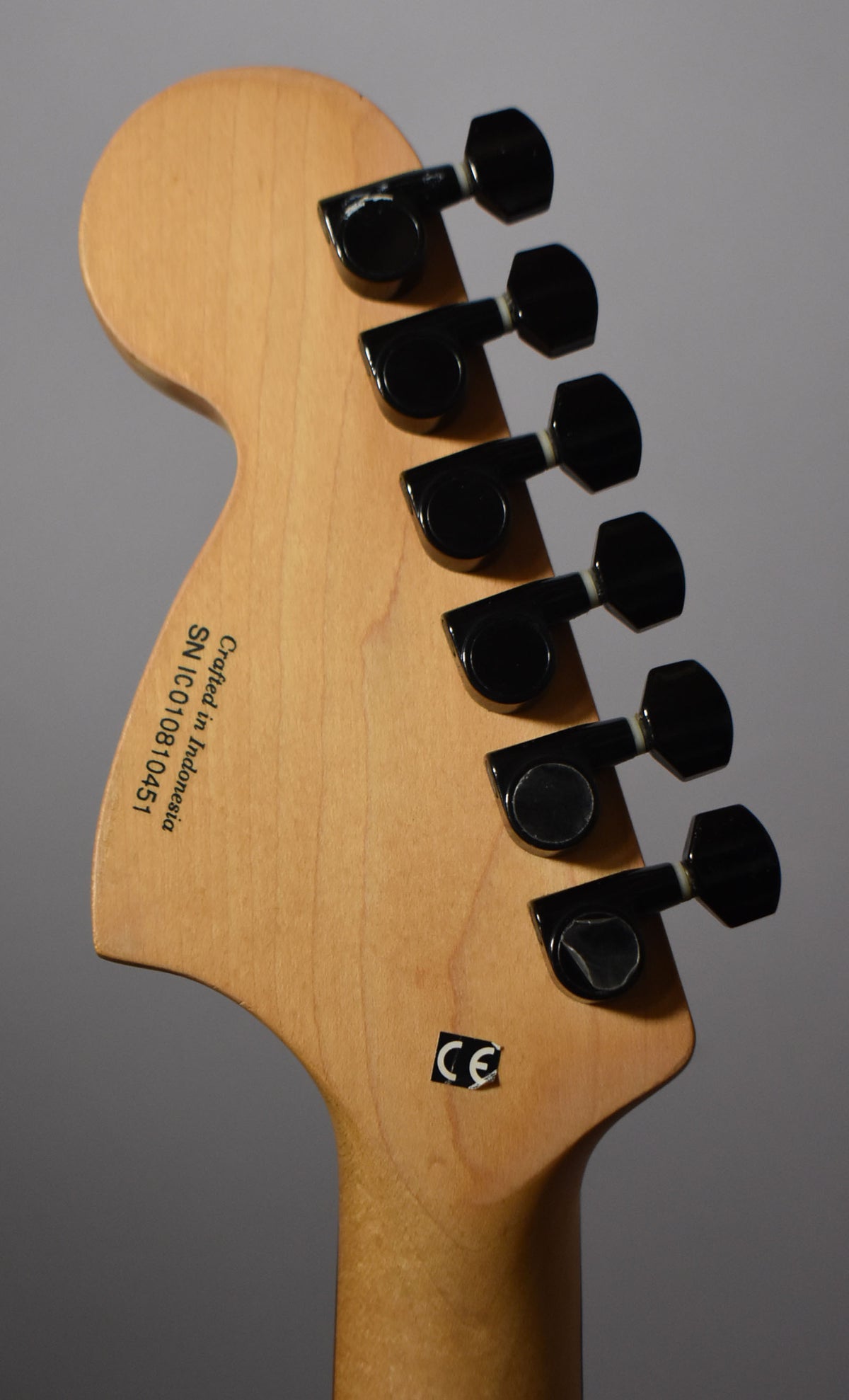 Rear view of the natural wood headstock and neck, showing six black tuning pegs and a "CE" sticker.