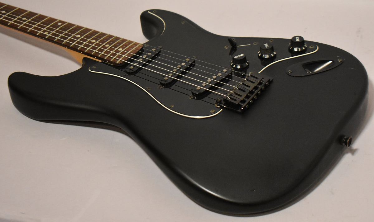 The black satin Stratocaster body is angled from the neck, showing a black pickguard, three black knobs, and a black tremolo bridge.
