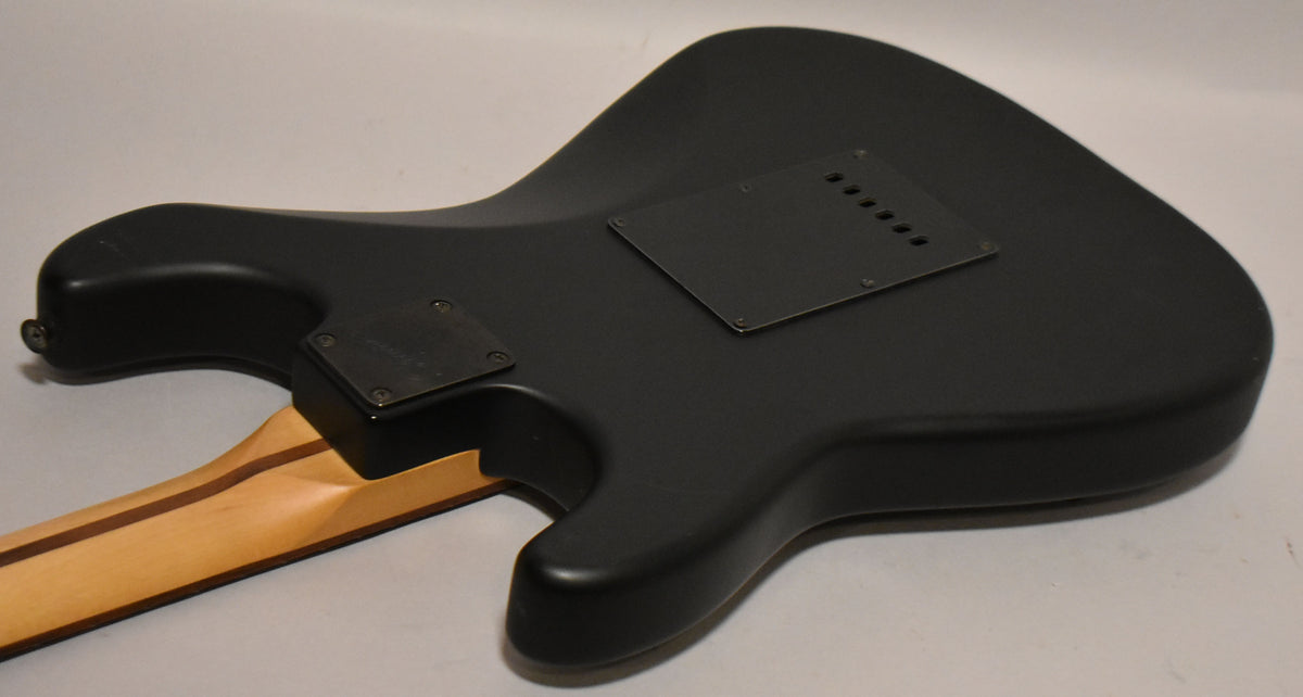 The guitar's satin black body is seen from the back, showing the neck joint and two black control cavity covers.