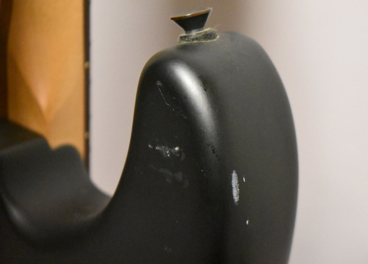 Close-up of the satin black guitar body's upper horn, showing a strap button and several white scuffs and scratches on the finish.