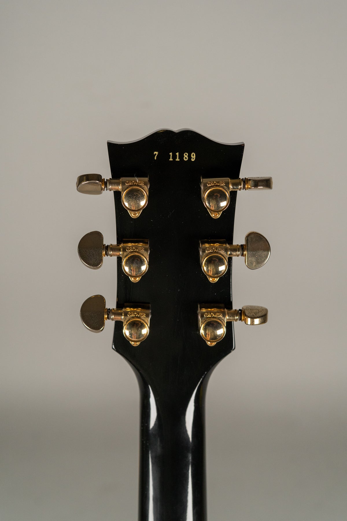 The guitar's black headstock, viewed from the rear, features six gold Grover tuners with some tarnishing and a gold serial number.